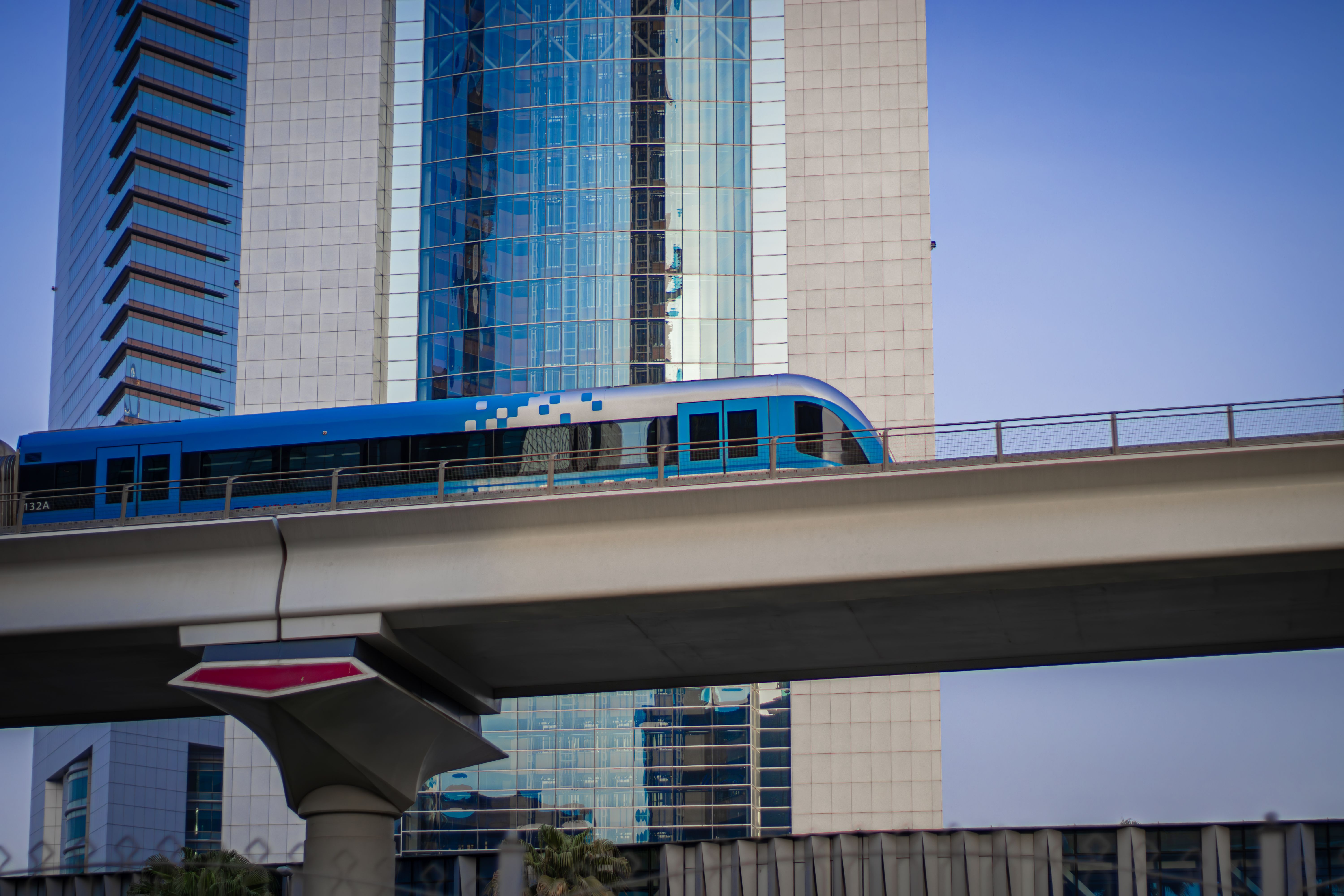 A sleek metro train passes high above a modern cityscape with tall glass skyscrapers.