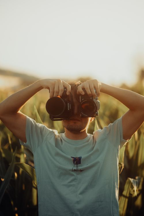 Free A man looking through binoculars while standing in a green field during sunset. Stock Photo