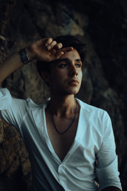 Free Profile of a young man in a white shirt leaning against a rock wall, exuding calmness. Stock Photo