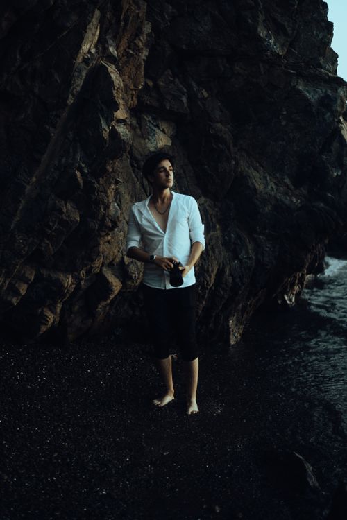 Free A man stands barefoot on a rocky shoreline, blending exploration with fashion. Stock Photo