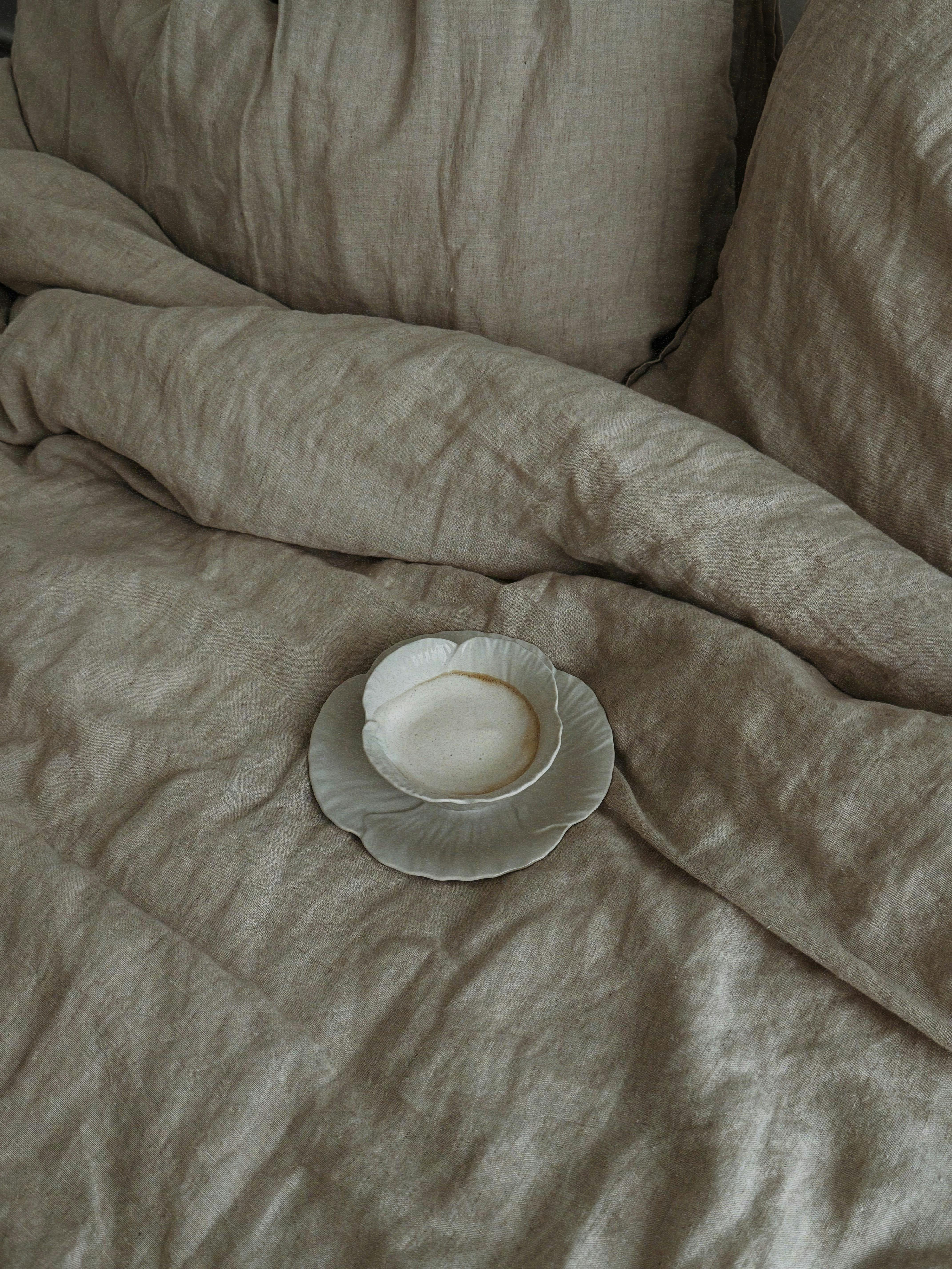 A rustic bedroom setting featuring vintage fabric bedding and a ceramic cup.