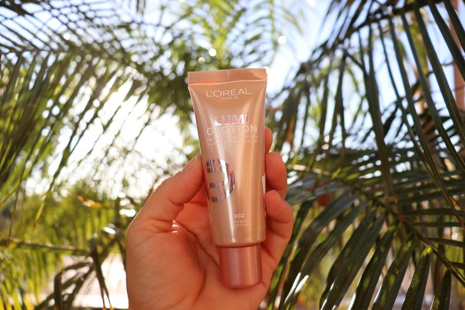 L'Oréal Lumi Glotion held by a hand with tropical palm leaves background, bright and vibrant.