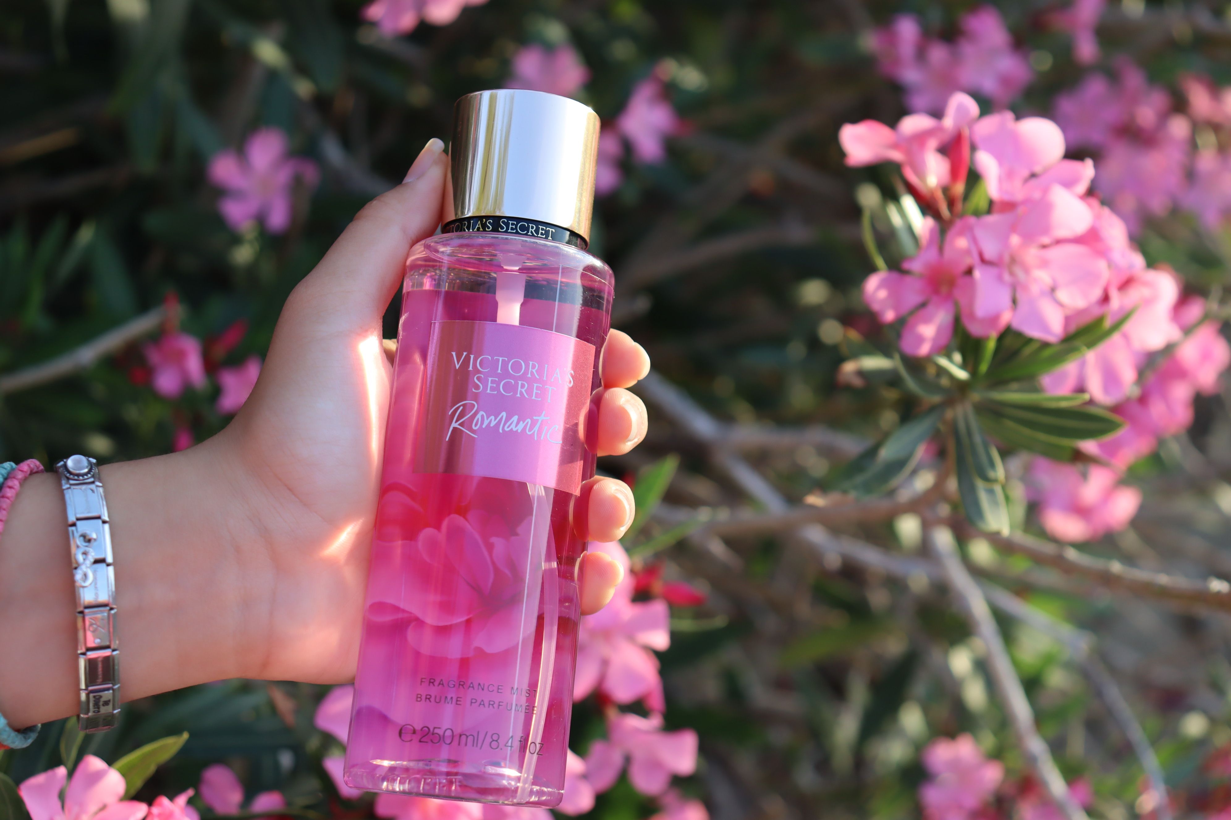 hand holding luxury perfume bottle surrounded by pink flowers representing natural fragrance ingredients