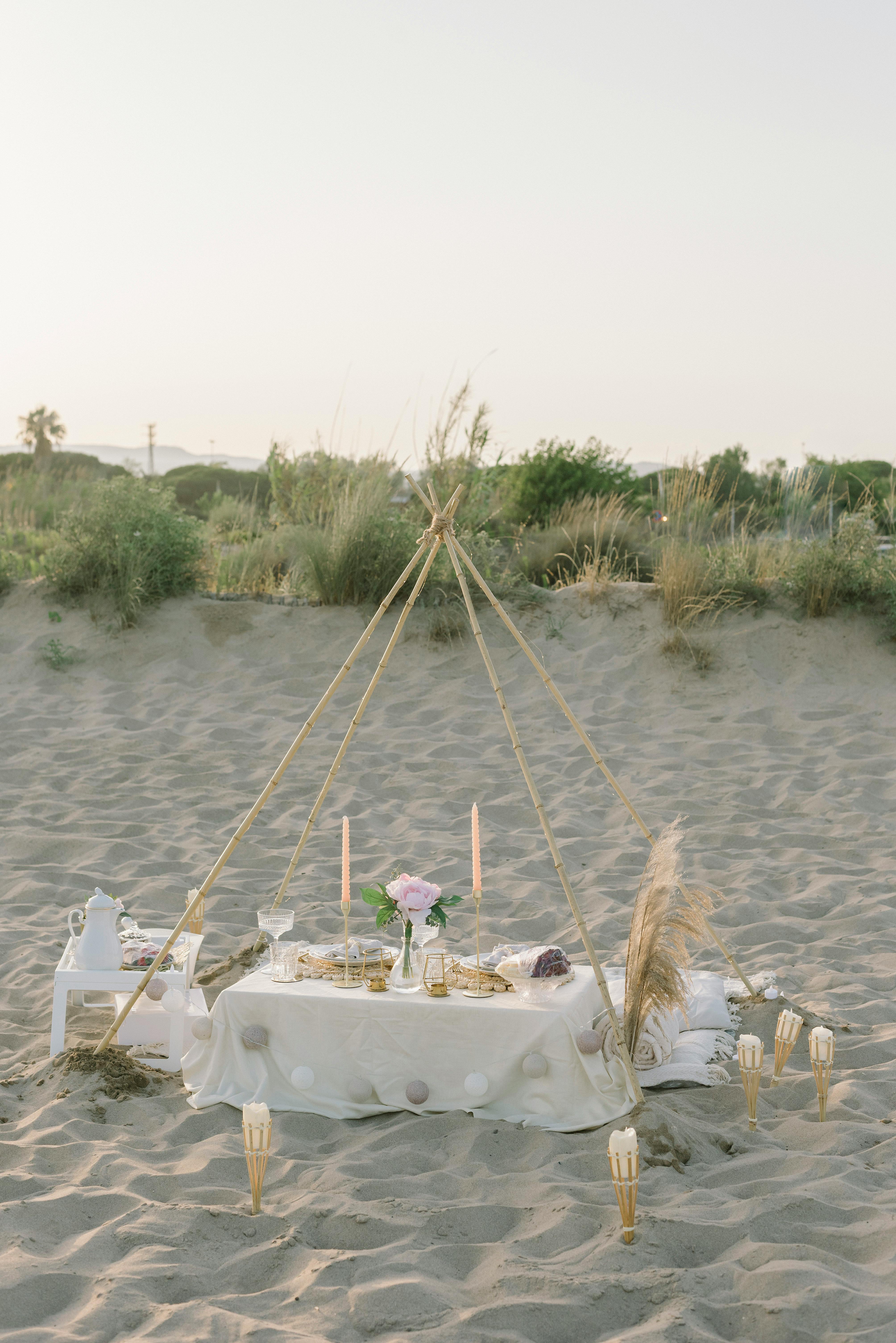 A serene beach picnic scene with a makeshift tent and elegant table setup on the sand.