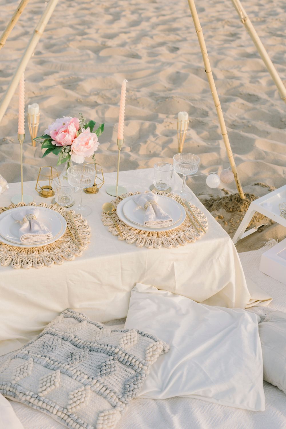 An intimate table for two on the sand with peonies, gold place settings and taper candles