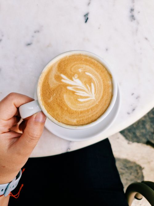 Free Cappuccino with intricate latte art held over a marble table, perfect for coffee enthusiasts. Stock Photo
