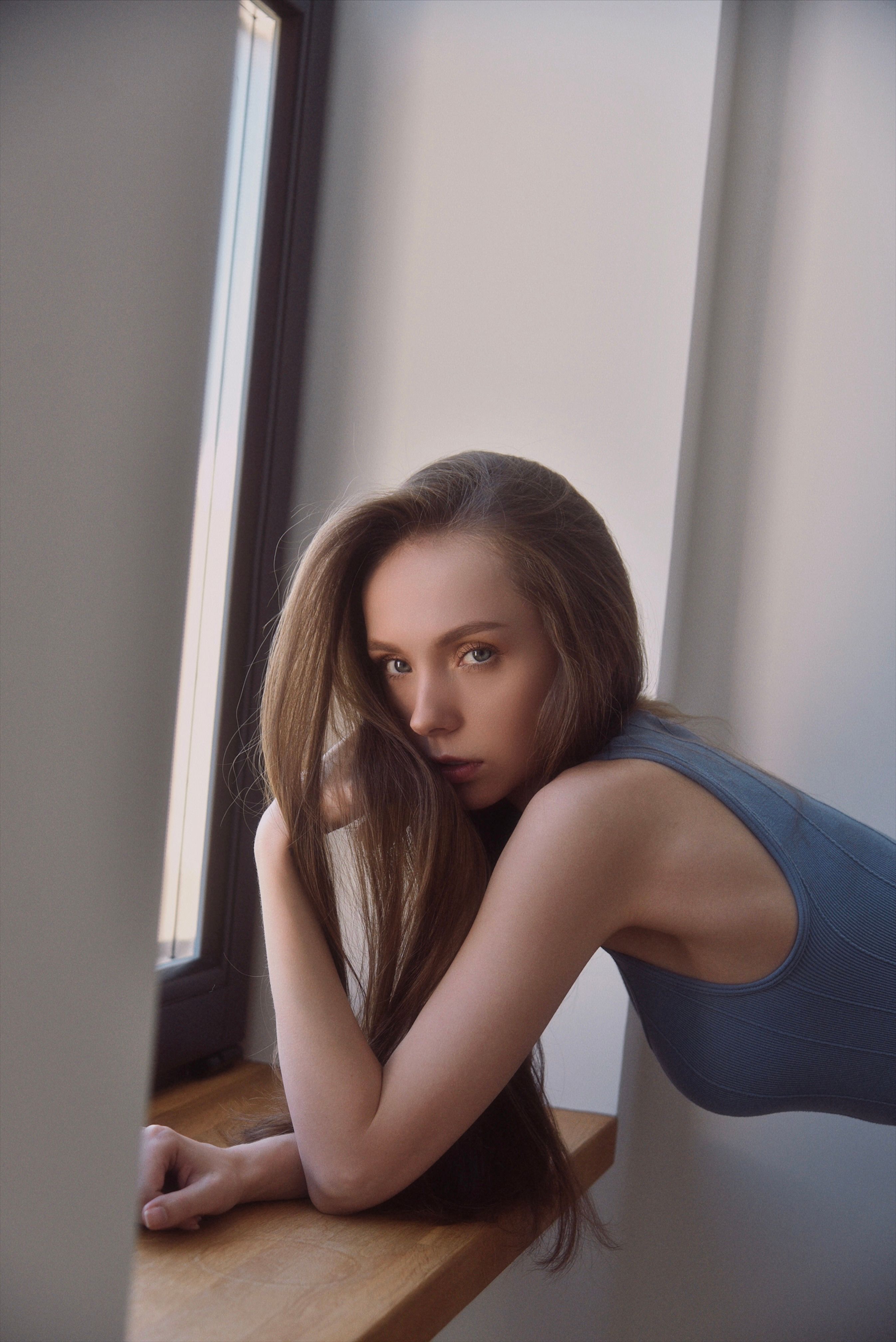 Young woman leaning by a window, reflecting in natural light, in an indoor setting.