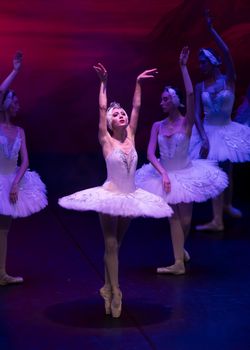 Ballet dancers performing in elegant white tutus under dramatic lighting.