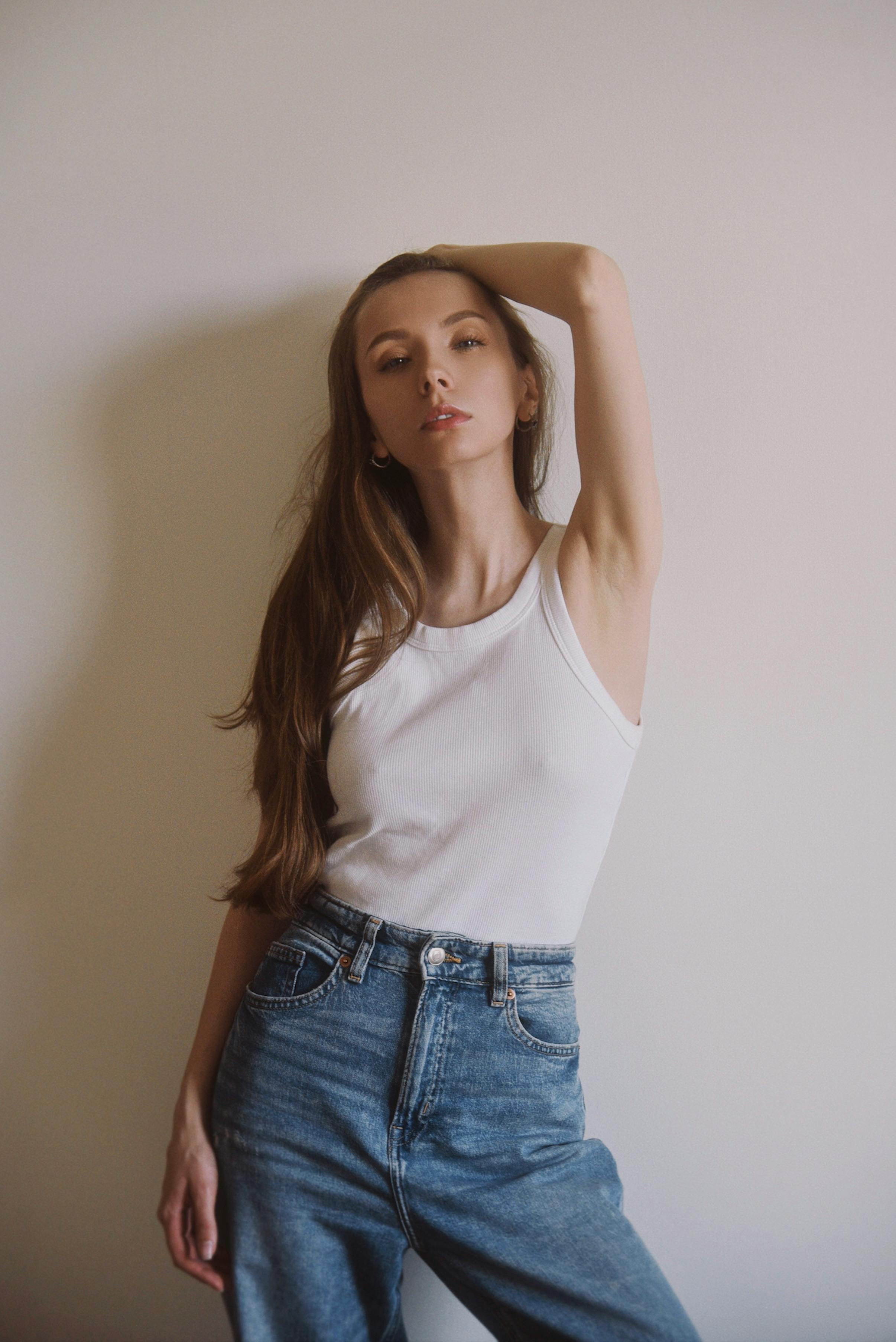 Portrait of a young woman in a white top and denim jeans posing casually indoors.