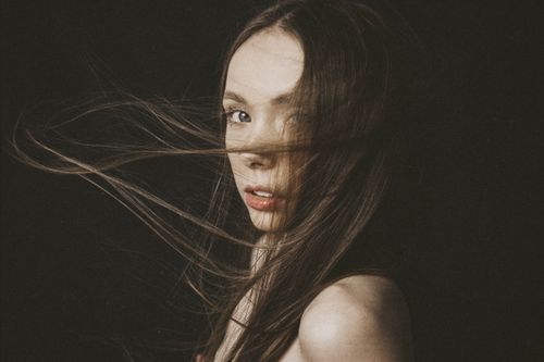 Free Artistic portrait of a woman with wind-swept hair, set against a dark backdrop. Stock Photo