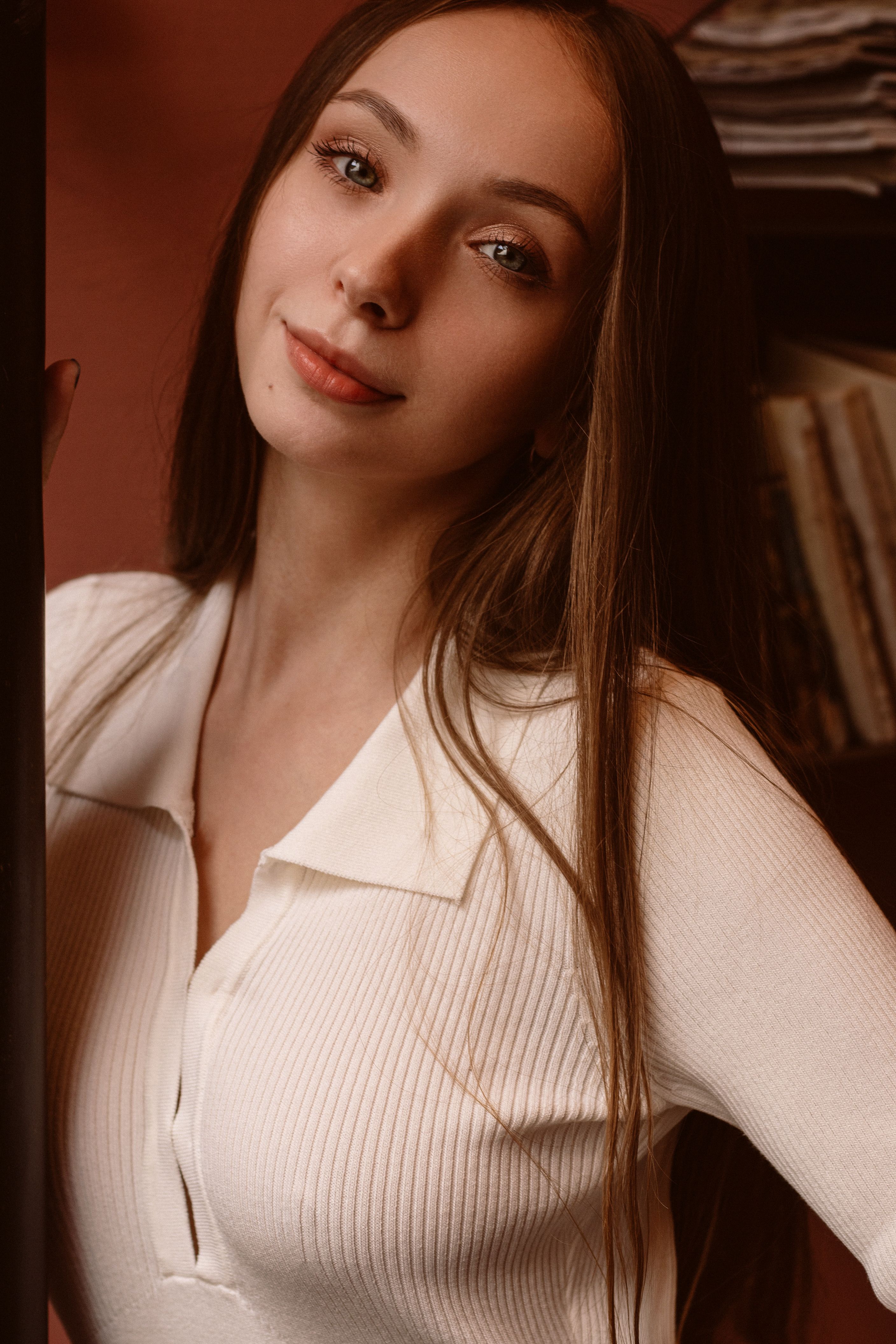 A captivating portrait of a young woman with long hair in a white top indoors.