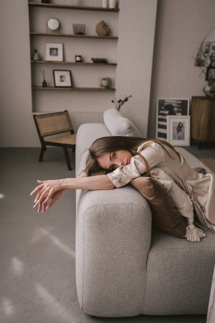 A woman in a satin robe relaxes on a sofa in a chic, minimalist living room with elegant decor.
