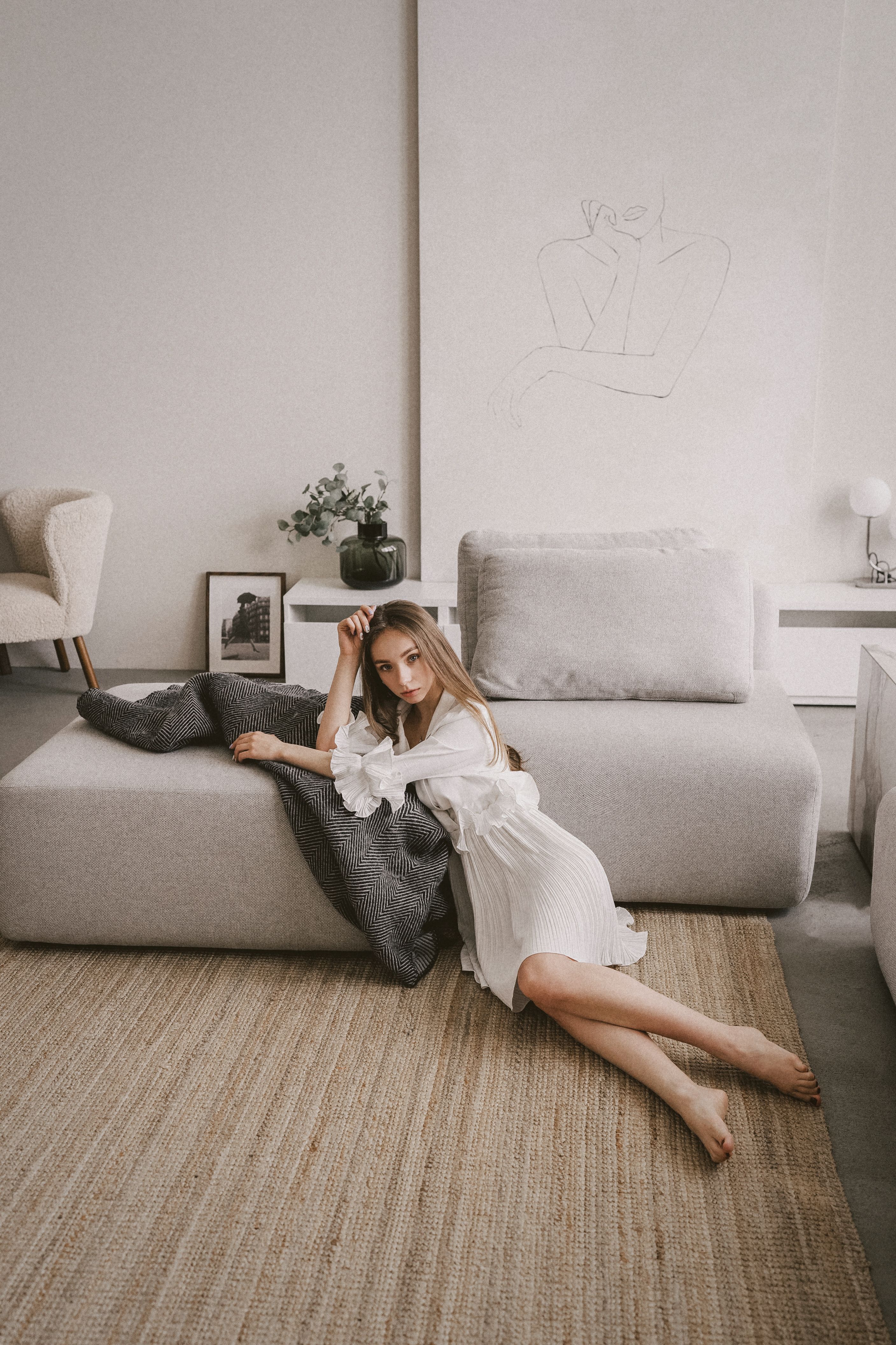 A woman in a white dress lounging on a modern couch in a stylish living room, embracing comfort.