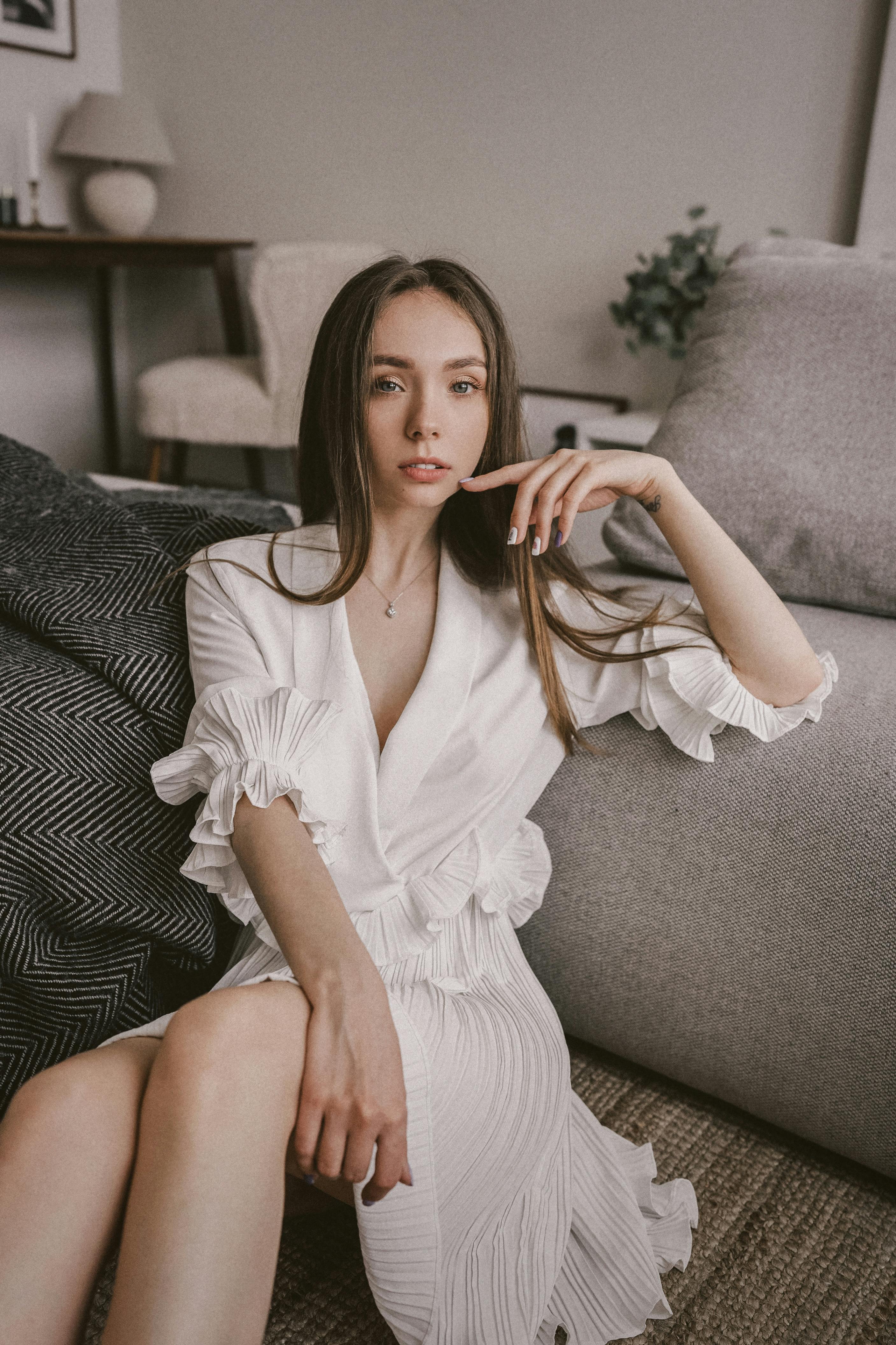 Portrait of a woman in a white dress seated in a stylish indoor setting.