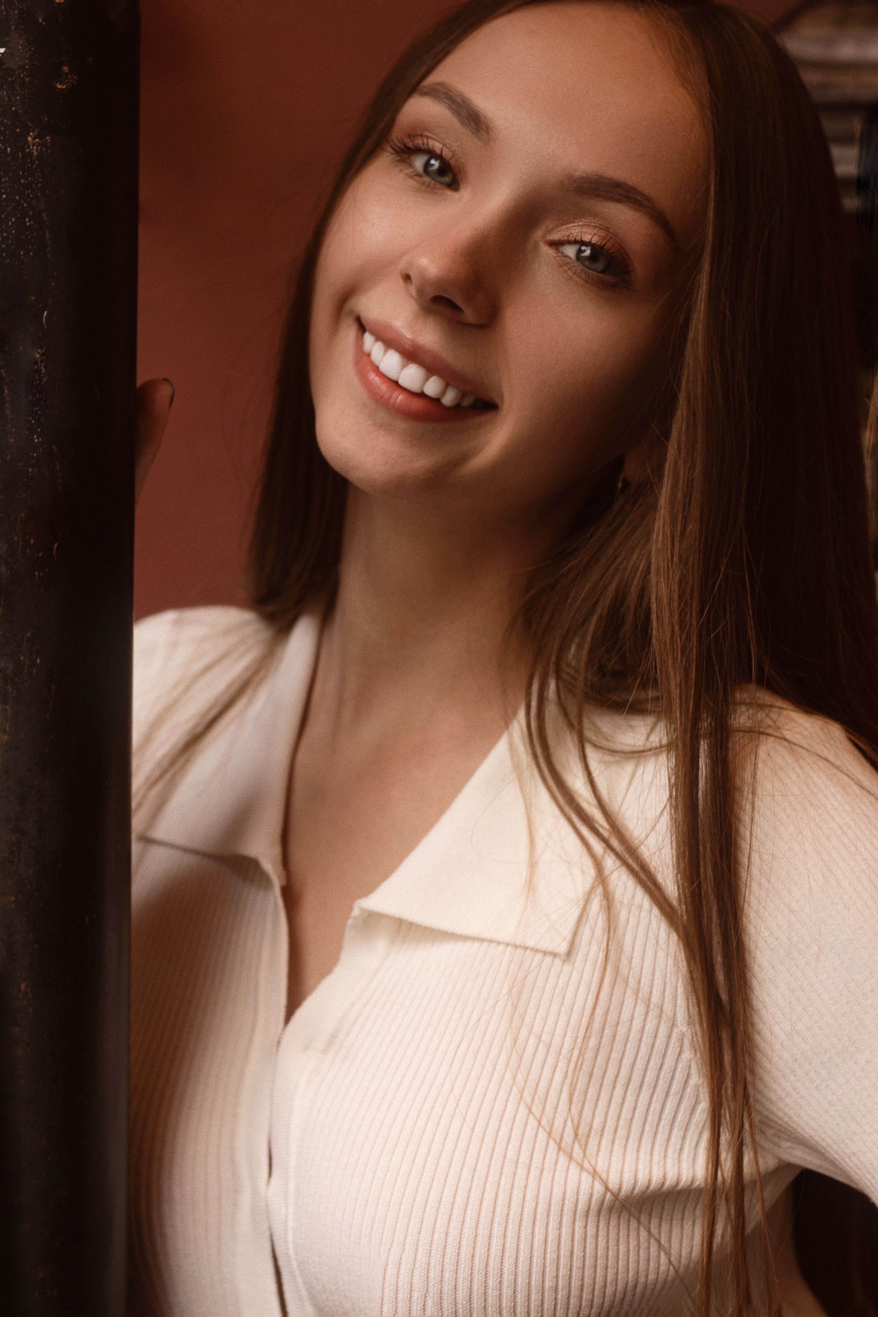 Portrait of a young elegant woman smiling indoors, showcasing a casual yet glamorous style.
