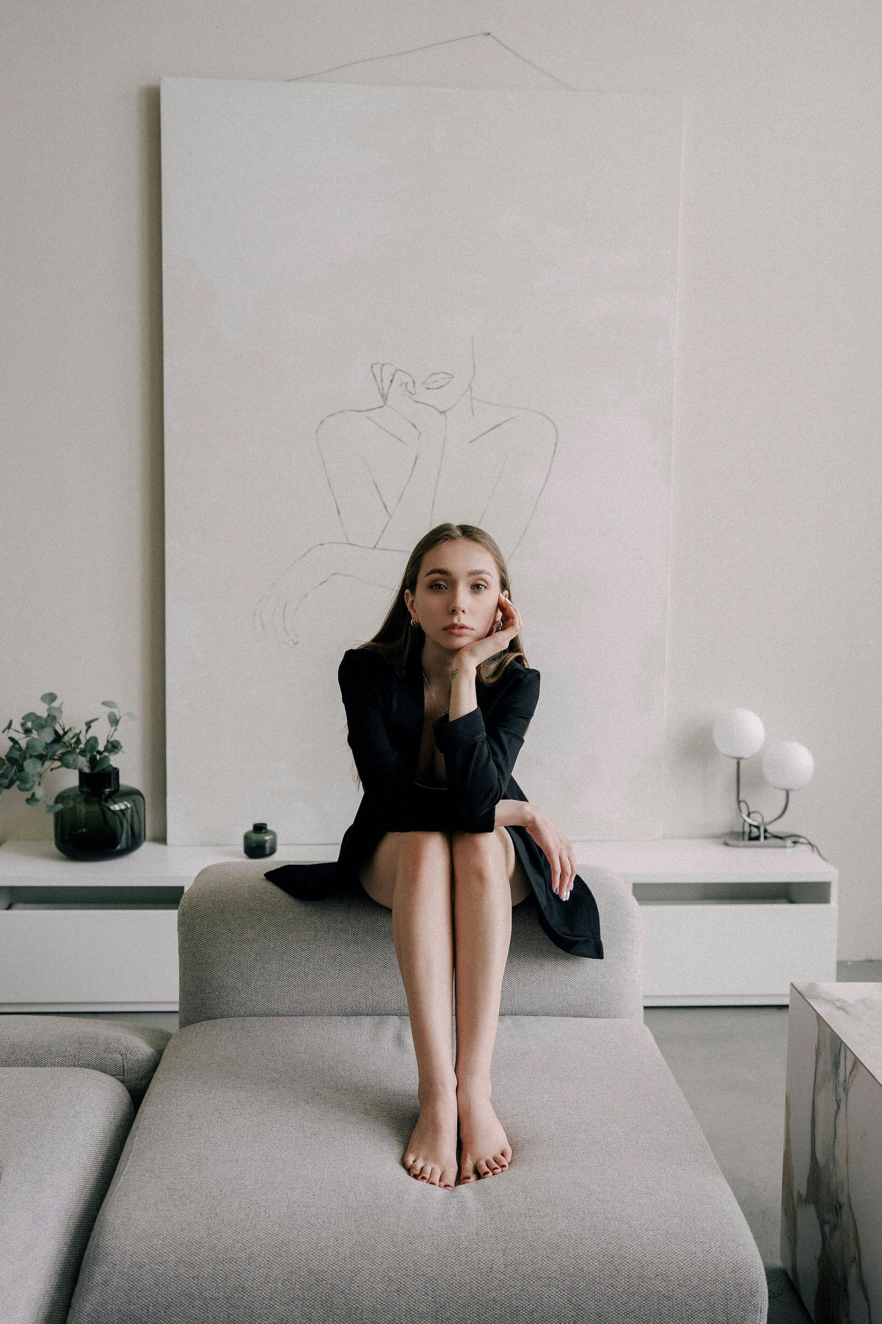 Stylish woman in black dress sitting gracefully on a modern sofa in a chic indoor setting.