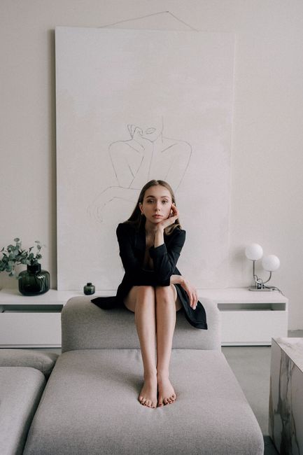 Stylish woman in black dress sitting gracefully on a modern sofa in a chic indoor setting.
