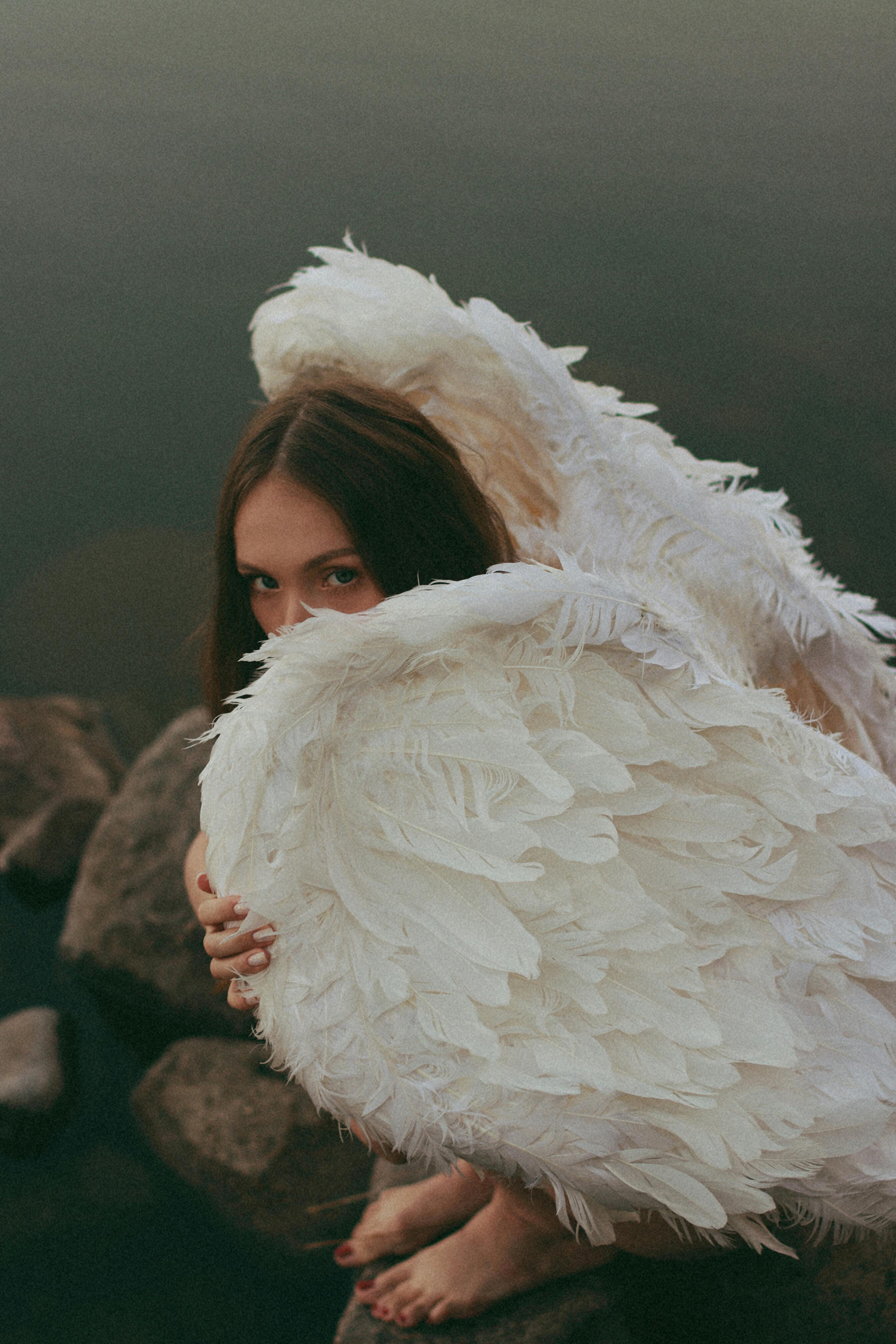 A woman with large angel wings sits by the water's edge, invoking a serene and mystical atmosphere.