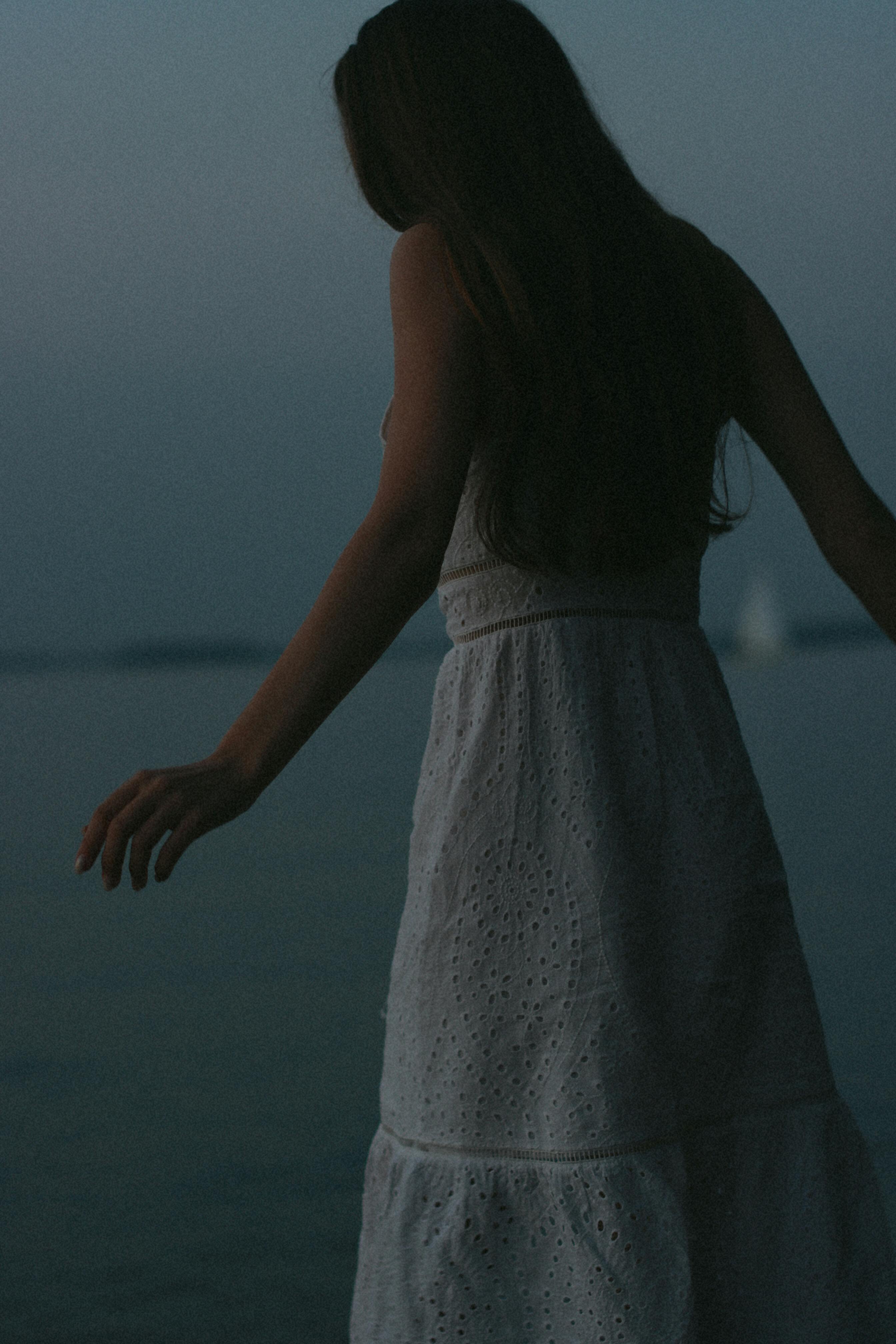 Moody evening silhouette of a woman in a white dress with a calm sea backdrop.