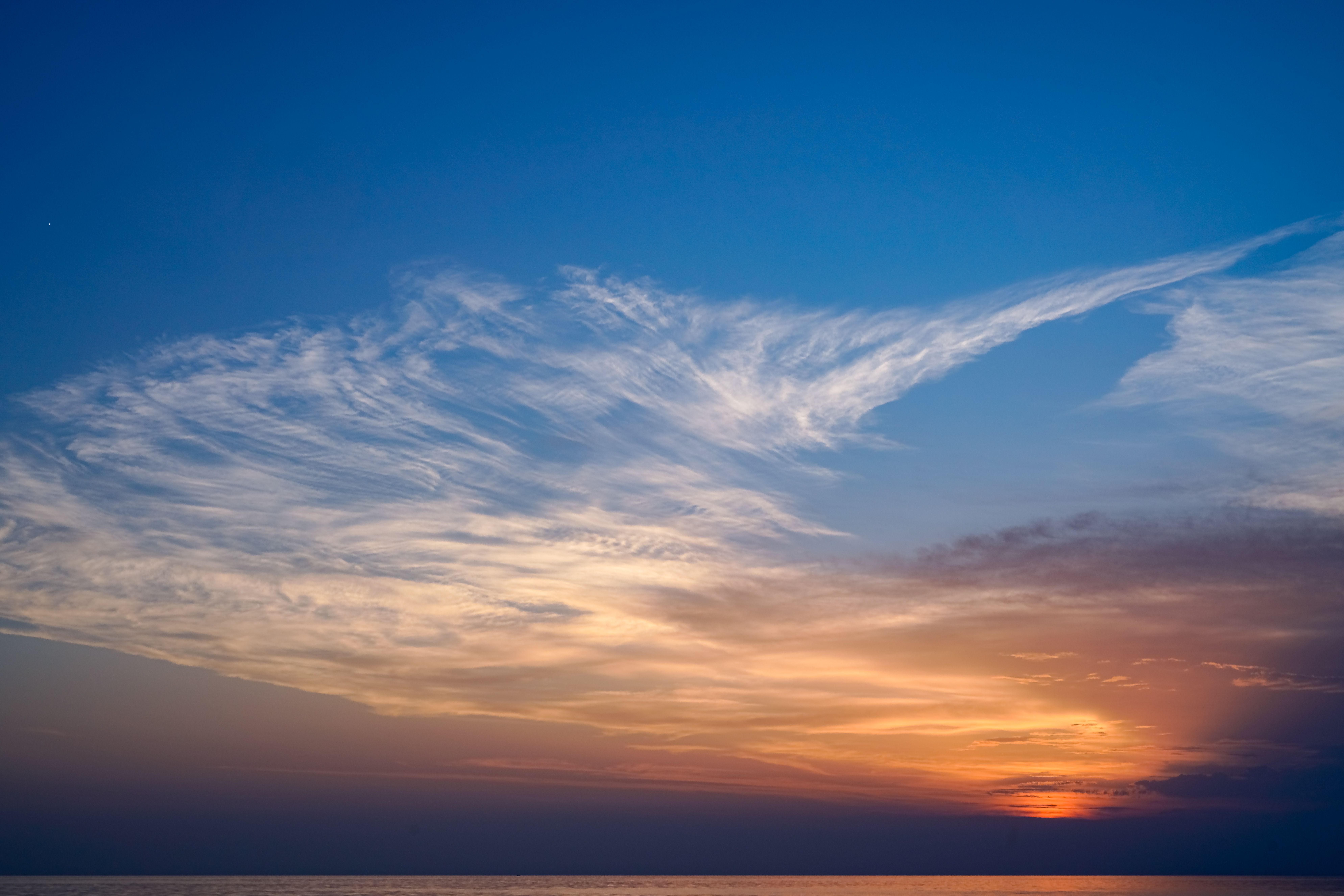 A sunset over the ocean with clouds in the sky · Free Stock Photo