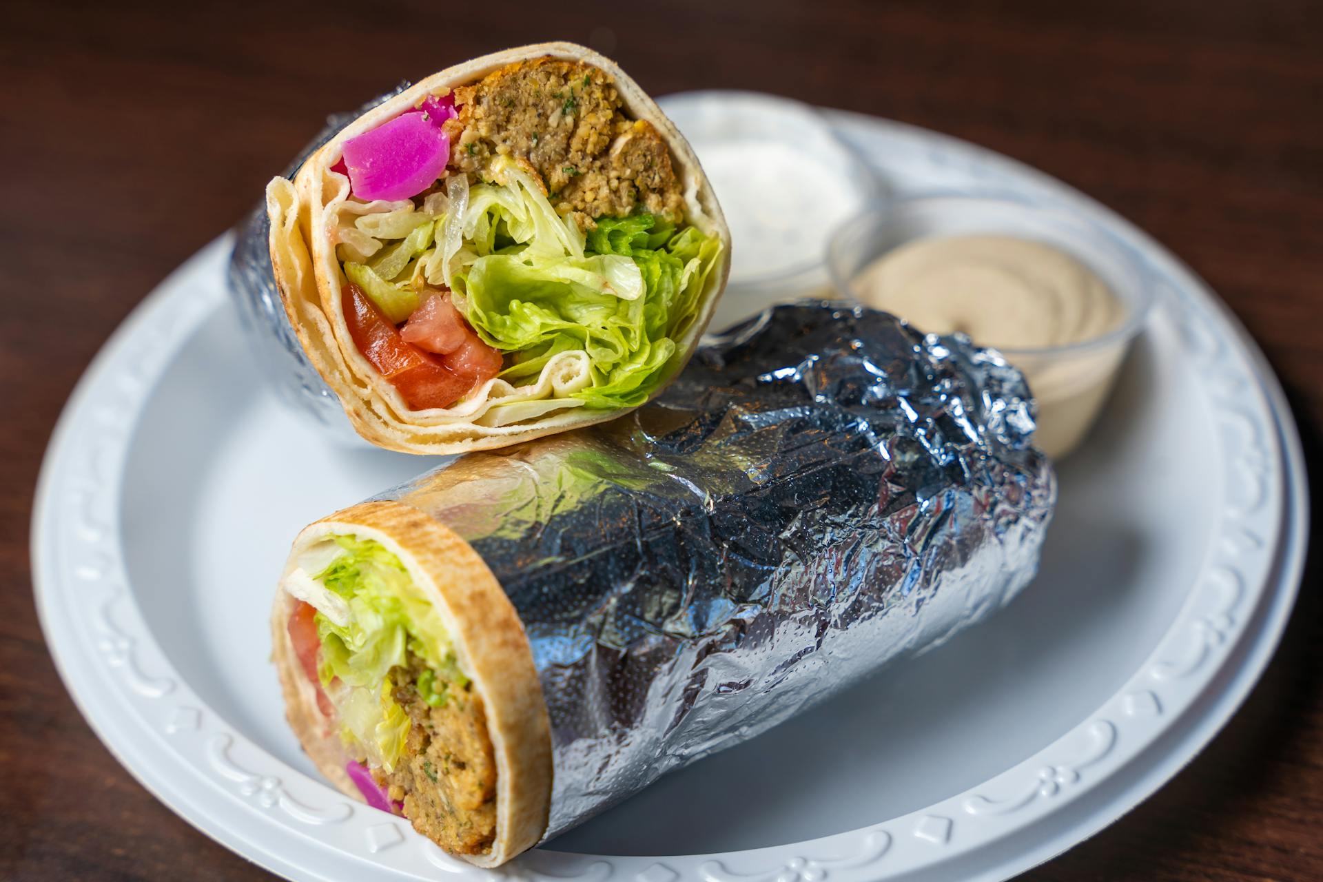 Tasty vegetarian falafel wrap with fresh vegetables on a white plate, ready to serve.