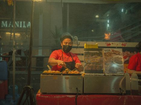 Street vendor preparing snacks at a night market in Manila; vibrant street food scene.