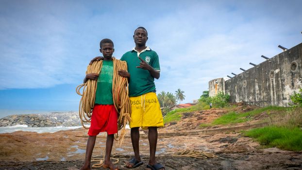 Two individuals holding rope on a seaside location with ruins in the background.