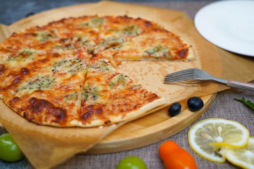 Delicious homemade vegetable pizza with herbs, lemon slices, and olives on a wooden board.