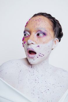 A creative artistic portrait featuring a woman with colorful face paint and a surprised expression.
