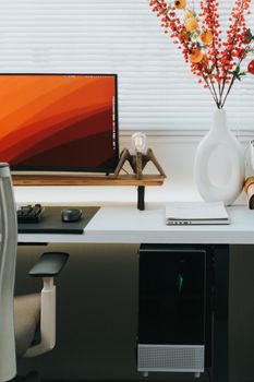 Stylish home office setting featuring a computer, ergonomic chair, and decorative vase with flowers.
