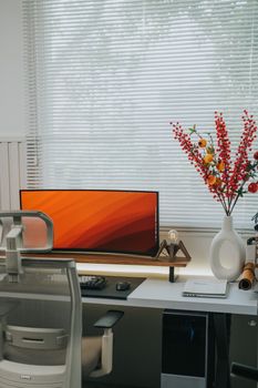 Stylish home office setup with a curved monitor, ergonomic chair, and vibrant floral arrangement.