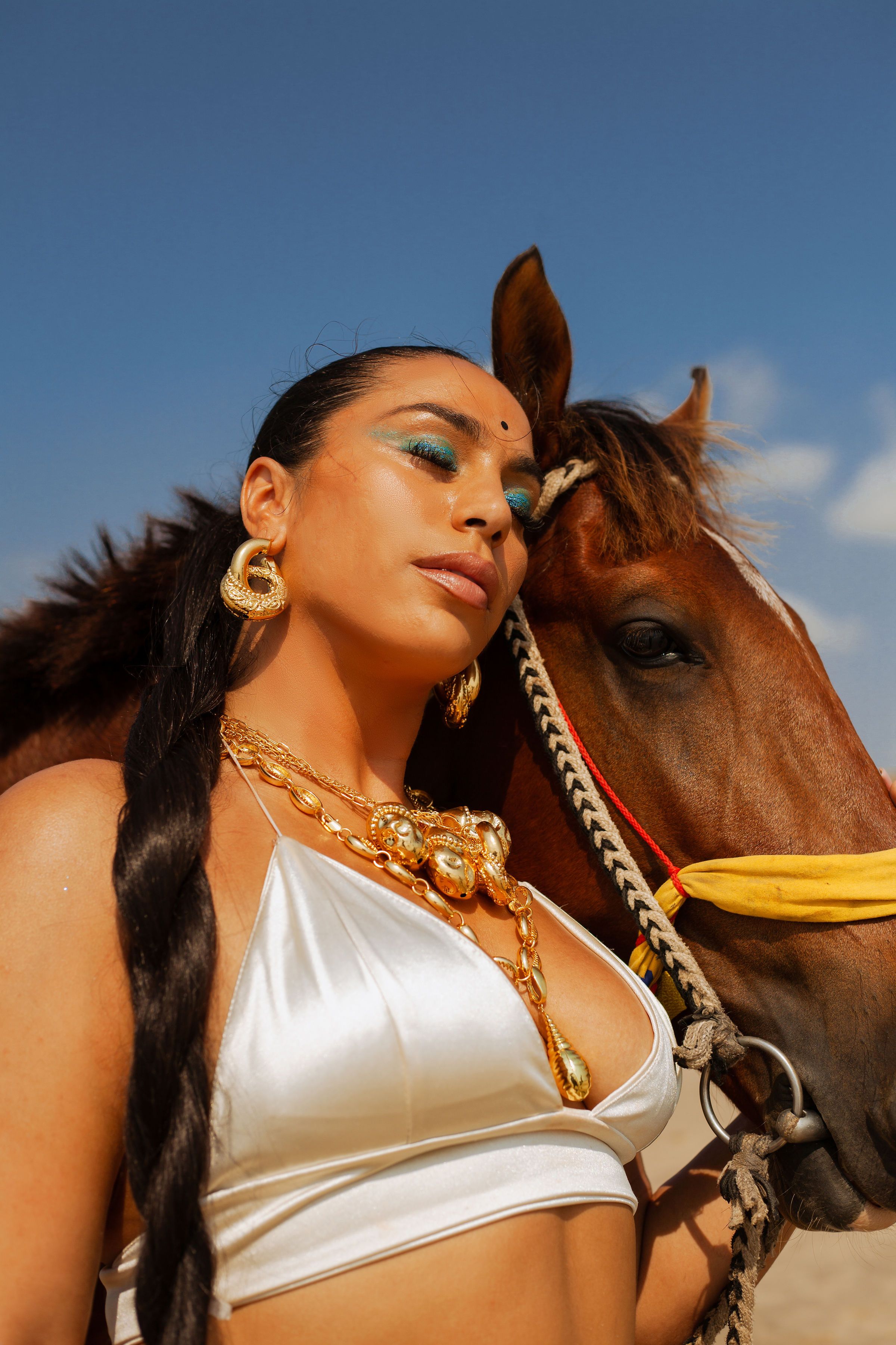 A woman in white top and gold jewelry is standing next to a horse ...