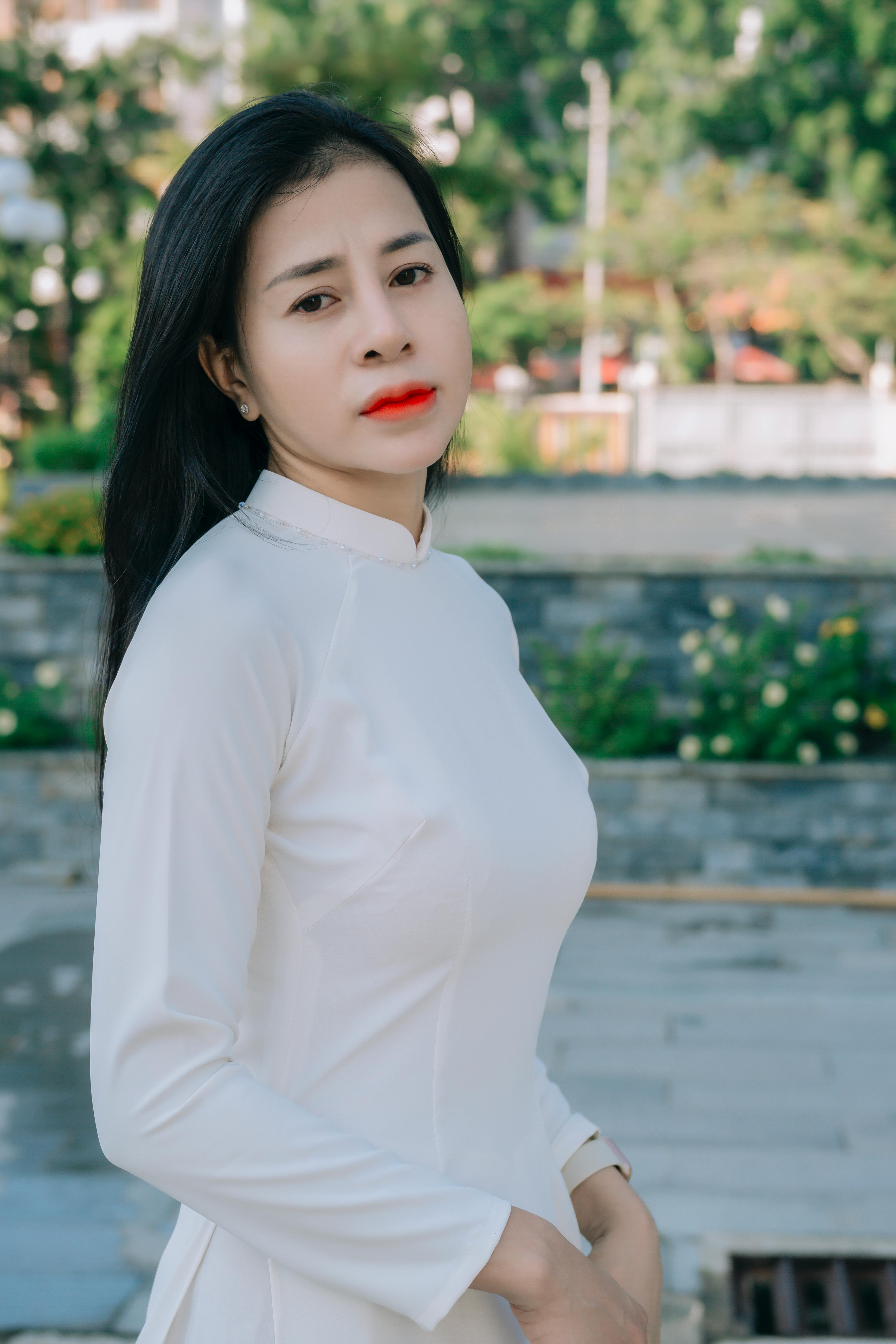 Portrait of a woman in a traditional white Ao Dai, standing outdoors during daytime.