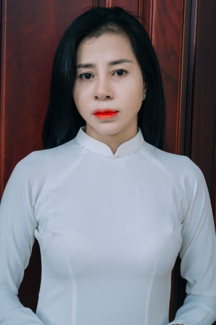 Woman in white traditional dress with red lipstick posing indoors against a wooden backdrop.