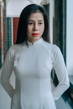 Portrait of a woman wearing a traditional white dress standing indoors, with a serene expression.