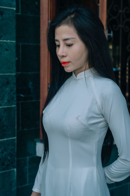 Portrait of a woman in a white Ao Dai with long black hair standing outdoors.