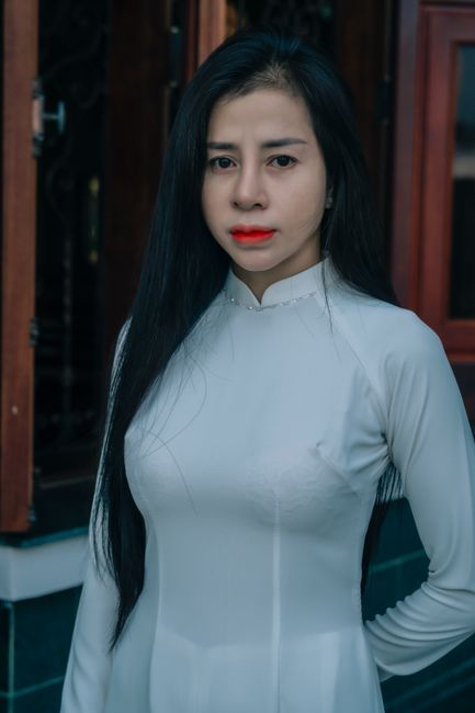 A portrait of a woman wearing a traditional white Ao Dai, standing outside.