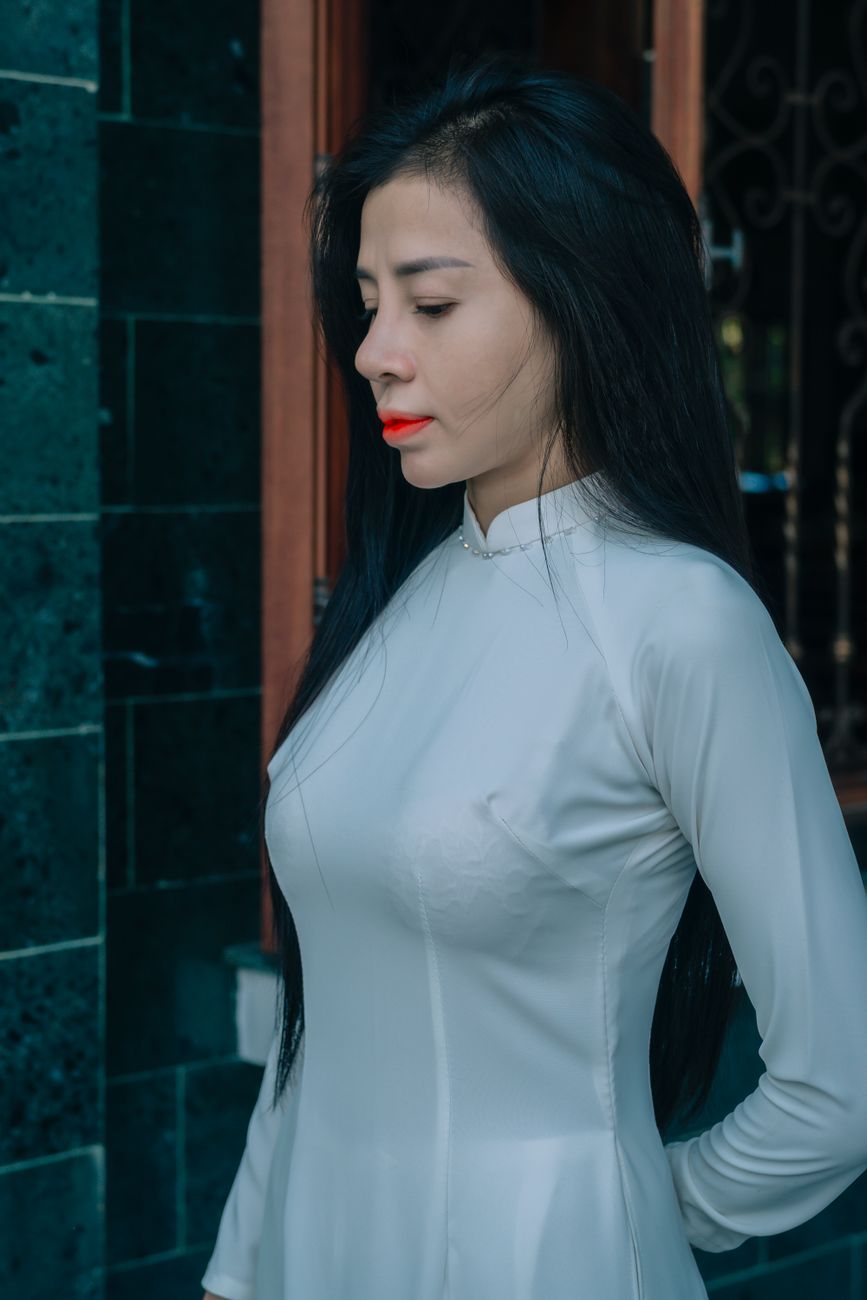 A serene portrait of a woman wearing a traditional white Ao Dai dress outdoors.