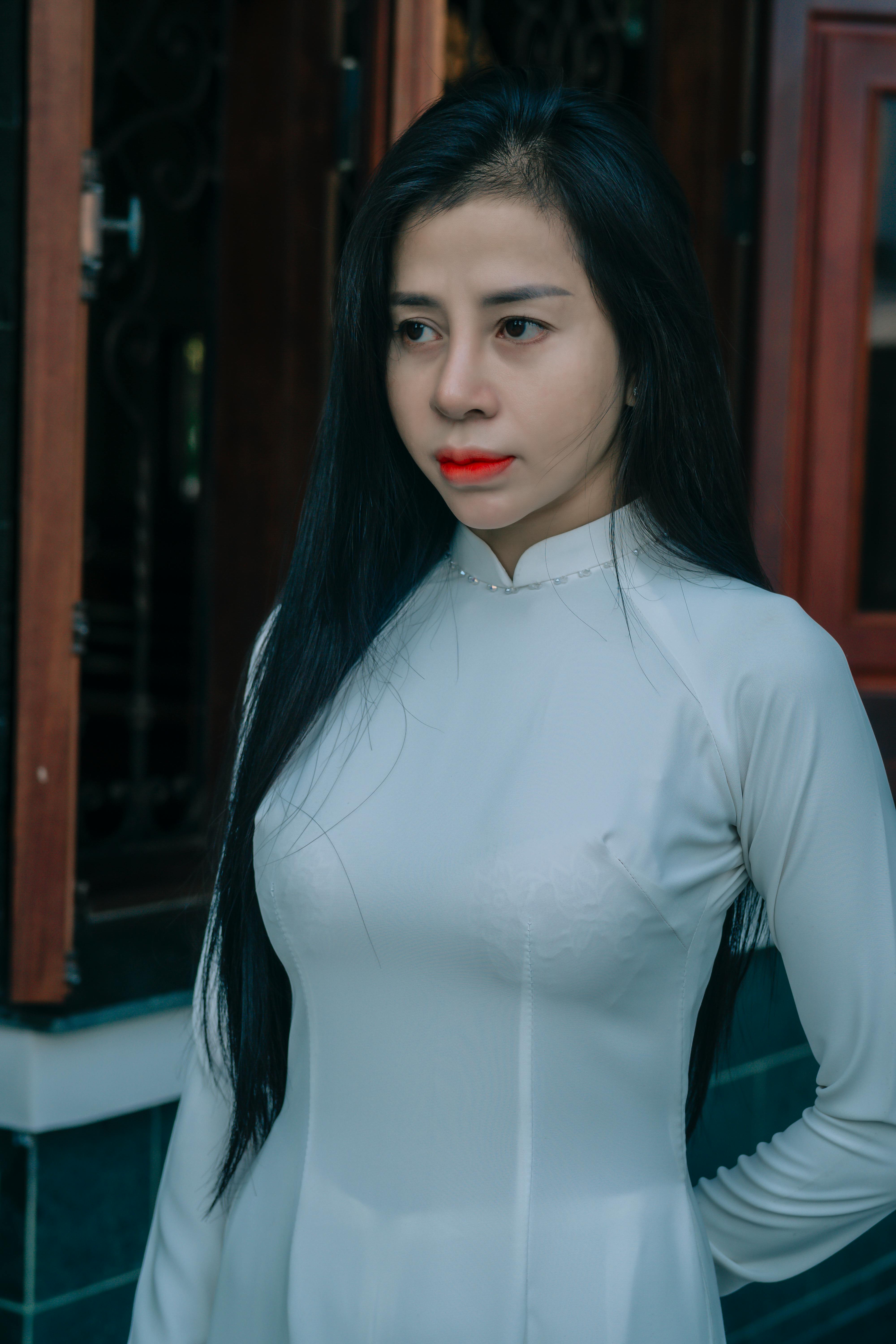 Charming portrait of a woman in white traditional attire standing near a wooden window.