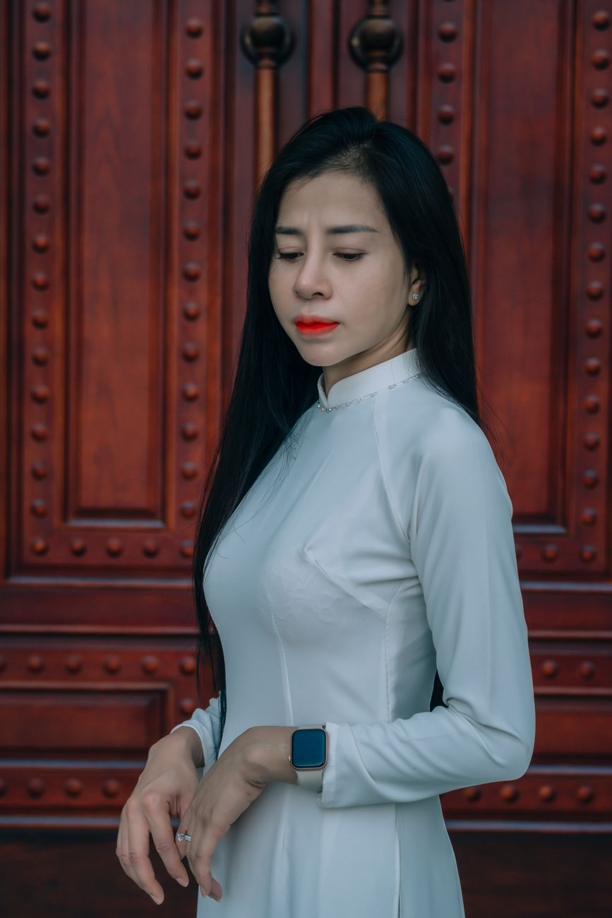 Portrait of a woman in a white Ao Dai standing before a prominent wooden door, exuding elegance and grace.