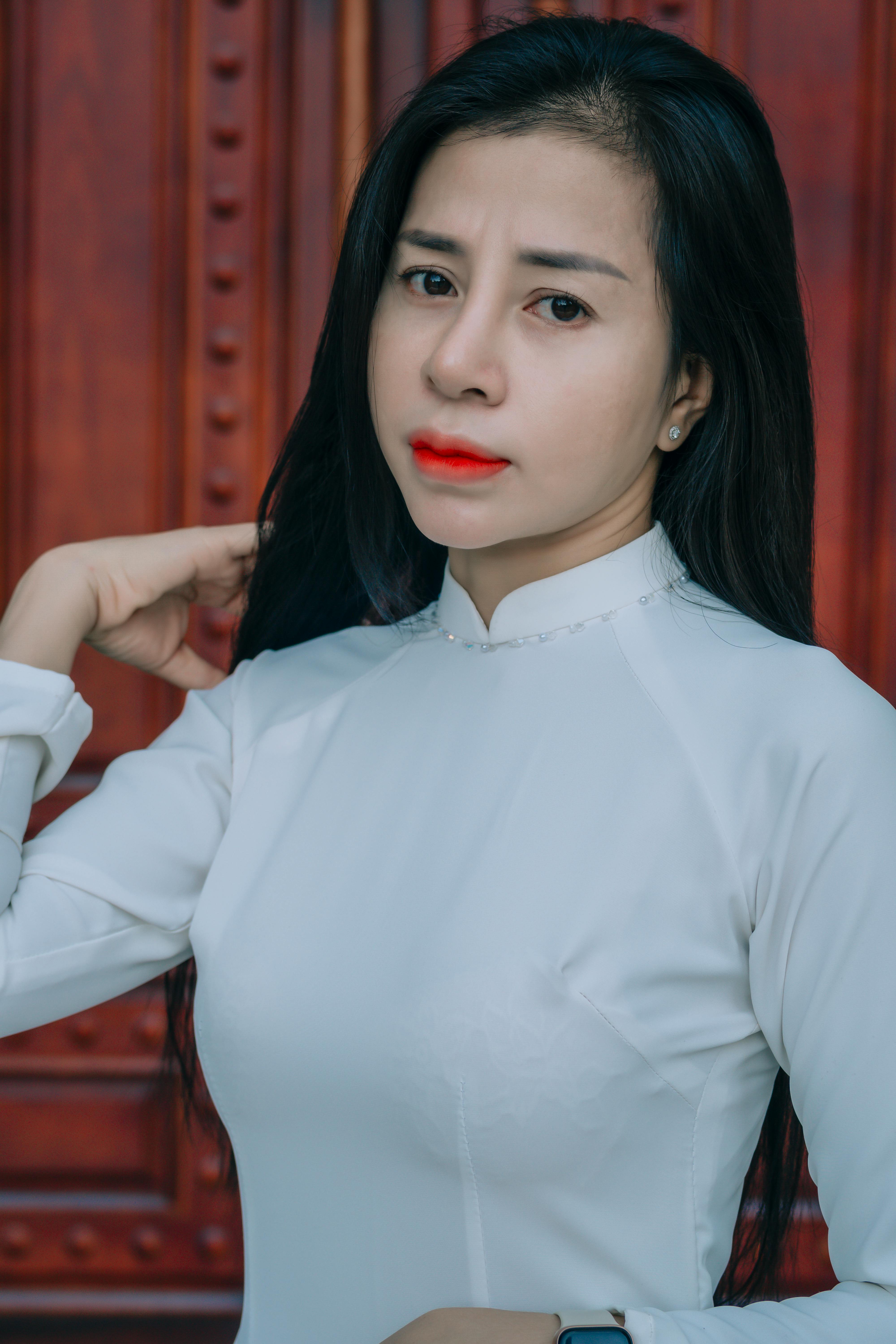 Elegant woman posing in a traditional white dress with a wooden background.