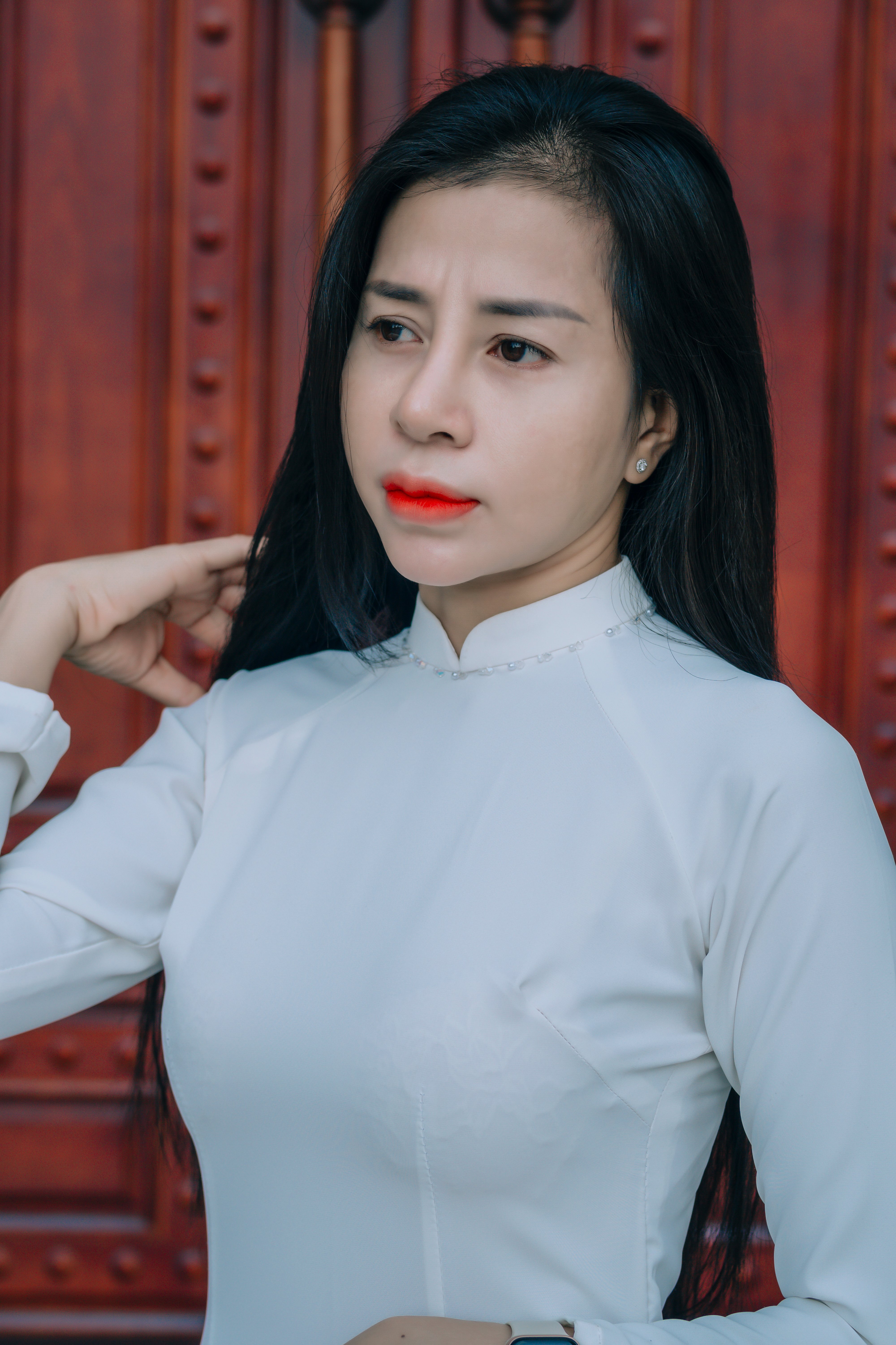 Portrait of a woman in white traditional attire with red lips standing against a wooden backdrop.