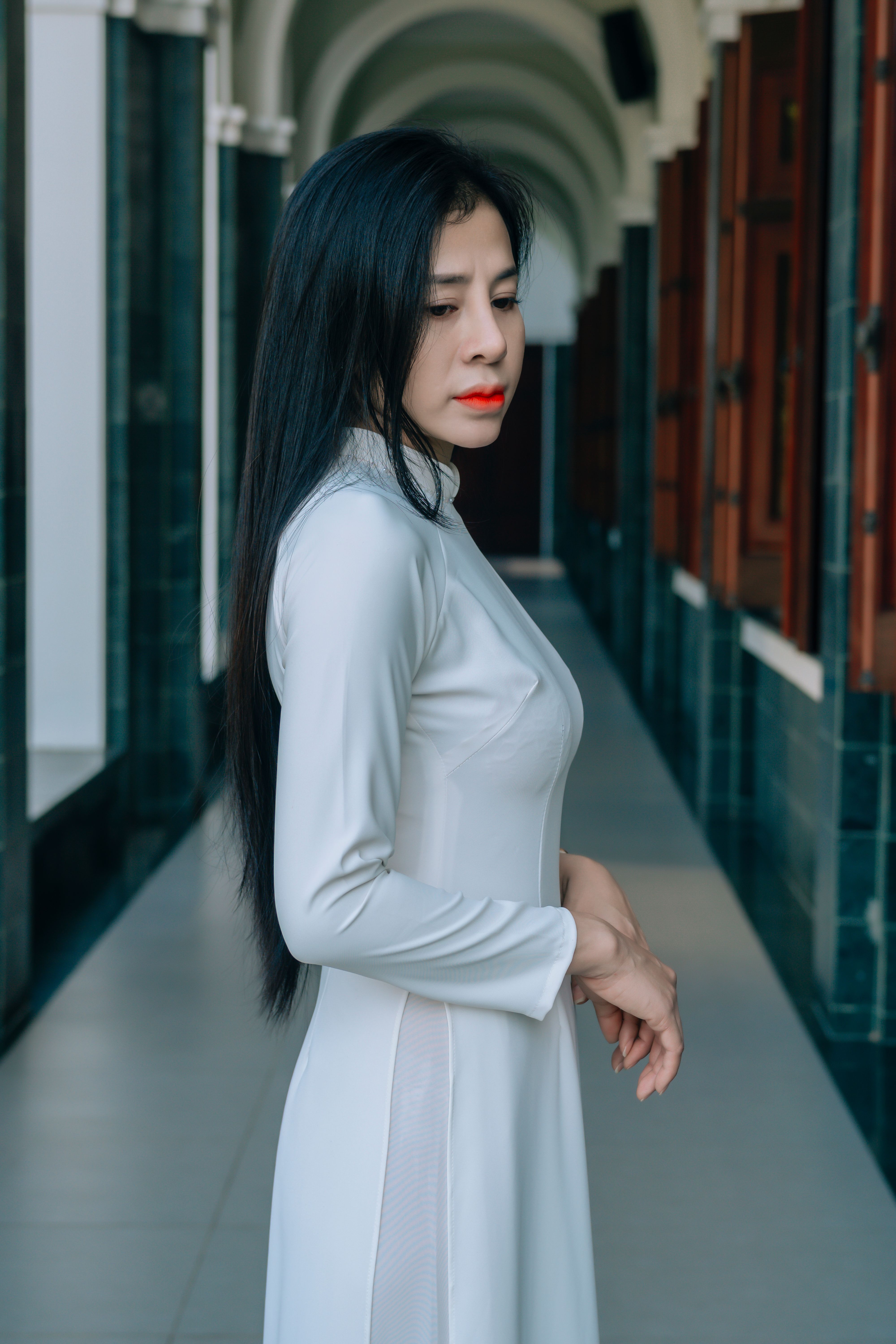 A woman in traditional long white dress poses gracefully in an elegant hallway.