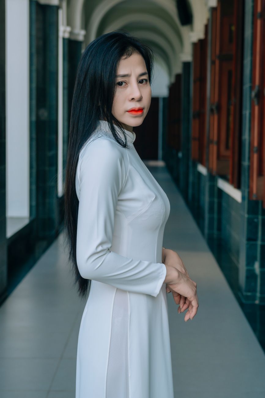 Portrait of a young woman in a sleek white dress standing in a hallway with arches.