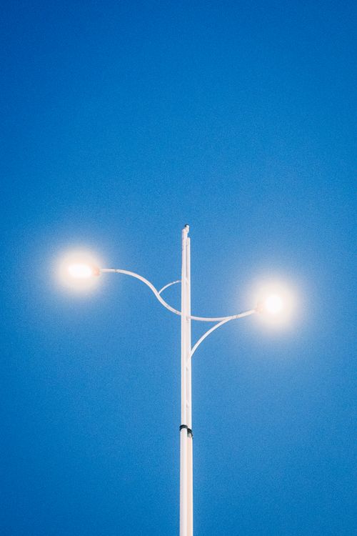 Free A modern street lamp illuminated against a bright blue sky, symbolizing energy and technology. Stock Photo