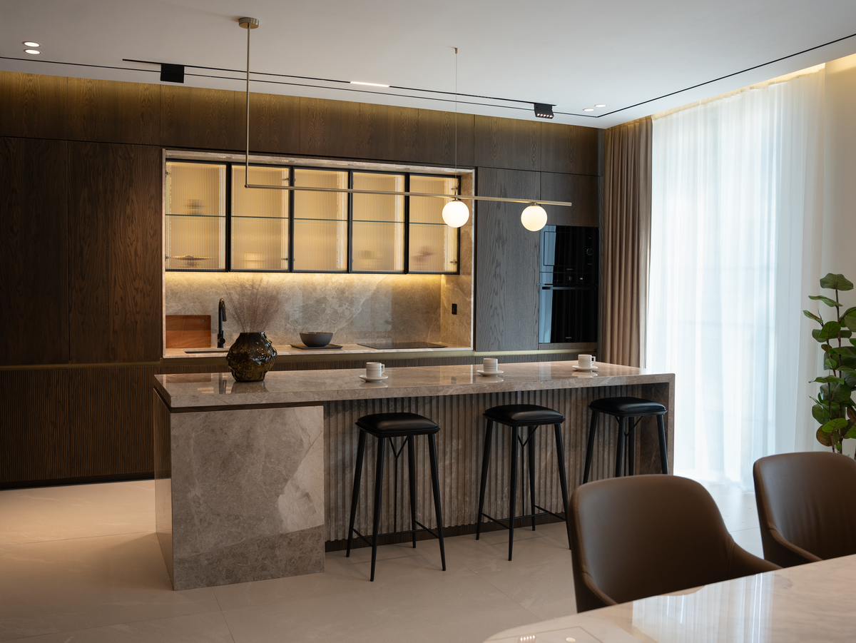 A dark kitchen with a stone island and bar stools
