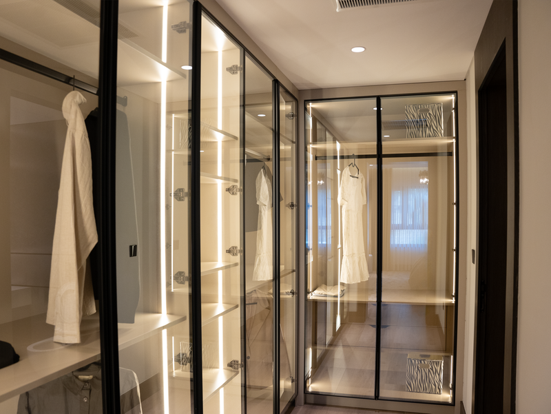 Stylish walk-in closet with glass doors and elegant lighting