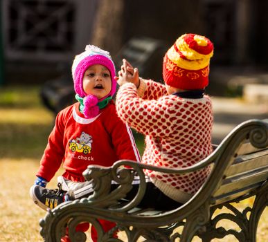 Two young children in winter attire enjoy a playful moment on a park bench.