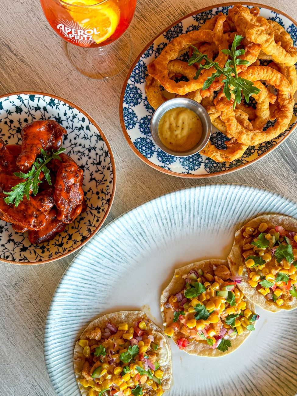 Assorted spicy American dishes including Nashville hot chicken, birria tacos, and Korean-style wings arranged on a restaurant table