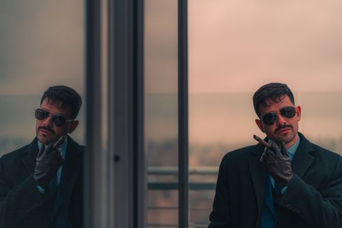 Free A fashionable man in sunglasses and coat reflected in a window, showcasing urban elegance. Stock Photo